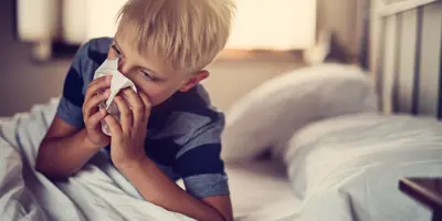 Blonder Junge mit Taschentuch auf der Nase