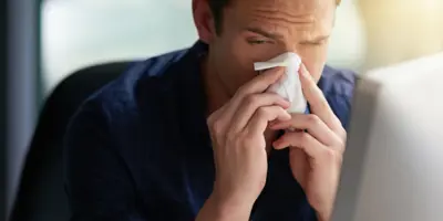 Mann in marineblauem Hemd schnäuzt sich die Nase