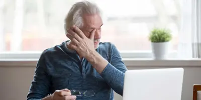 Älterer Mann sitzt vor einem Laptop und hat trockene Augen