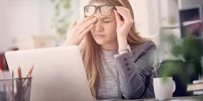 Eine junge Frau leidet unter tränenden Augen während sie an einem Laptop arbeitet