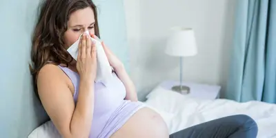 Een zwangere vrouw zit op een bed en snuit haar neus in een zakdoekje