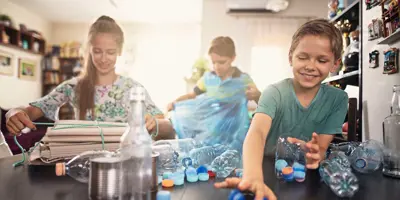 Drei Kinder lernen verschiedenes Plastik und Möglichkeiten zum Recycling kennen, indem sie es sich in der Küche ansehen