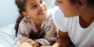 Una bambina e una donna sorridenti leggono insieme un libro su un letto.