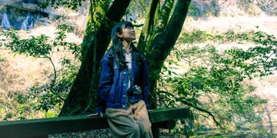 Eine junge Frau sitzt auf einer Bank in einem Wald und genießt die Natur während des Waldbadens.