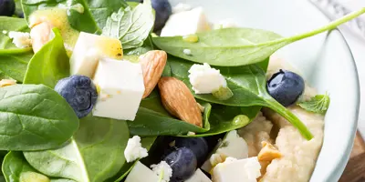 Frisch angerichteter Spinat Salat mit Heidelbeeren, Mandeln und Feta auf Bohnenpüree.