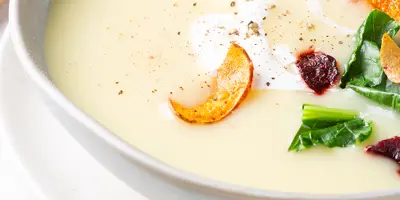 Cremige Kohlrabi Suppe in einer hellen Schale, garniert mit Gemüsechips, Crème fraîche und gemahlenem Pfeffer.