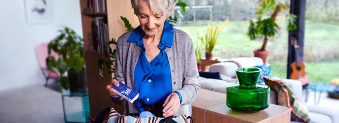 Eine ältere Dame hält eine Packung Tempo Taschentücher über einer gestreiften Handtasche, um sie einzupacken.